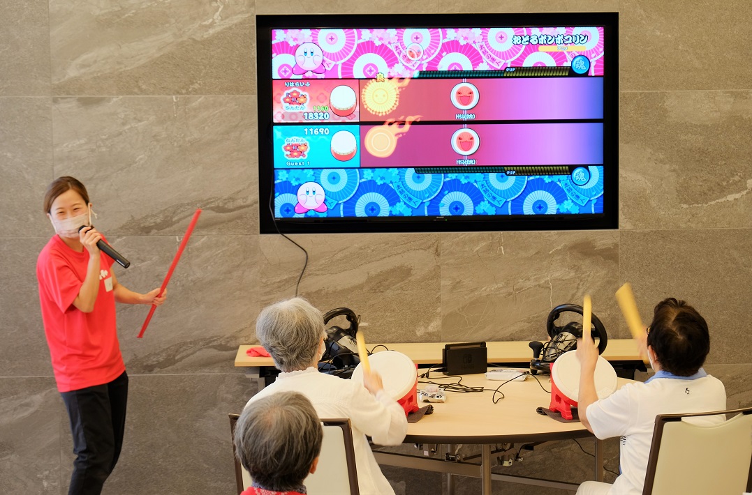 「太鼓の達人」でみんな笑顔に。左は健康ゲーム指導士の宮崎さん