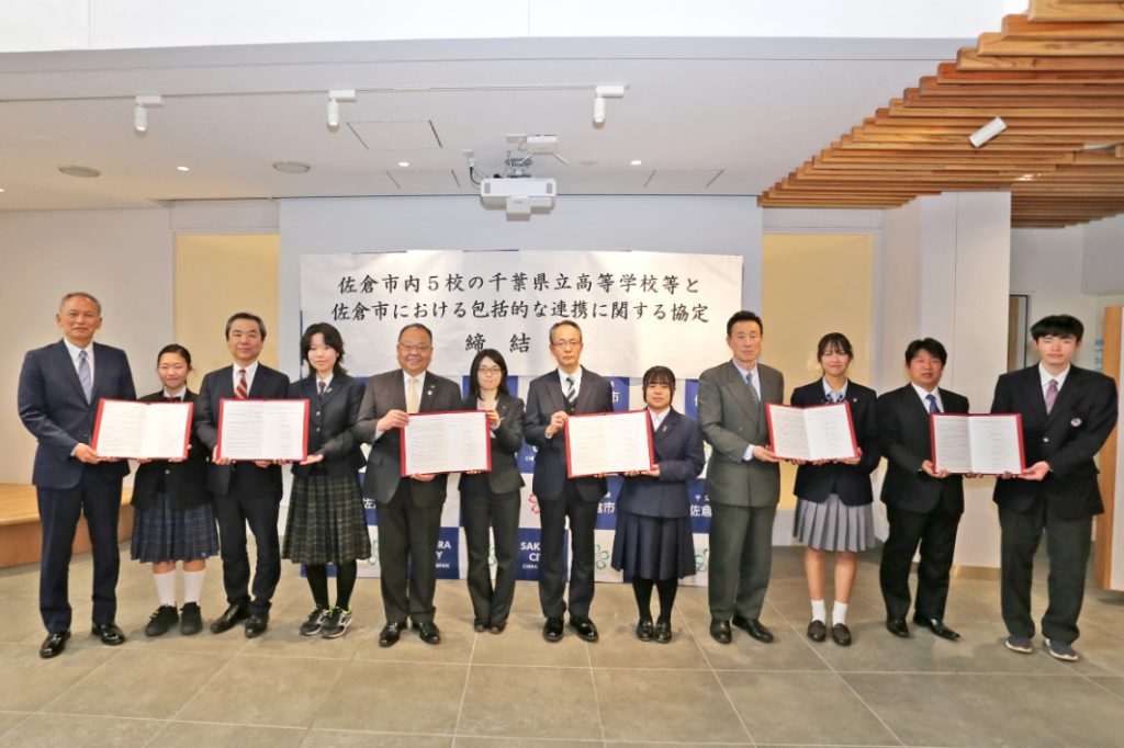 署名済みの協定書を掲げる市長、職員代表と各学校長、生徒代表