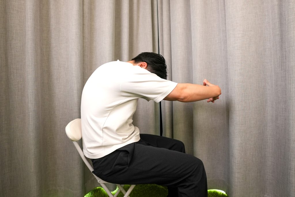 腕の前で手を組み、息を吐きながら背中を丸めて、手を前に伸ばす